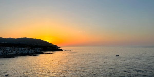Sunset over a calm sea with a small boat.