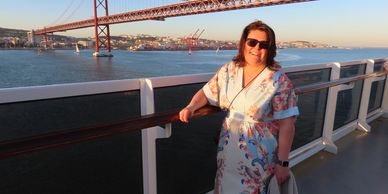 A woman in sunglasses posing on a boat with a red bridge and cityscape in the background.