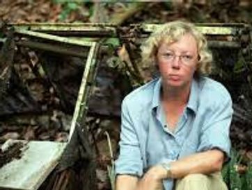 A woman with glasses sitting outdoors near an old, rusty structure.