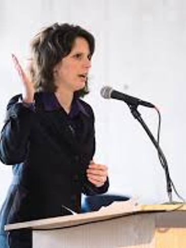 Woman speaking passionately at a podium with a microphone.