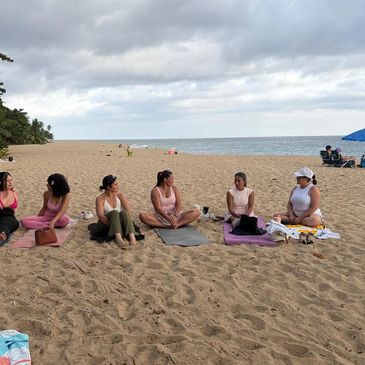 A group of women sitting on a sandy beach near the ocean.