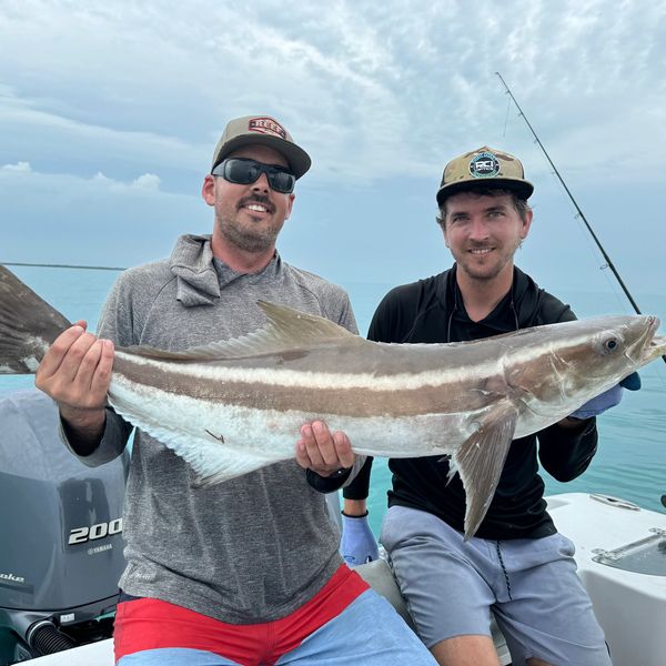 Two men on a boat holding a large fish.