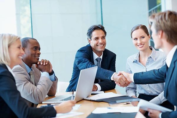 People sitting at a conference table with two men shaking hands in agreeent