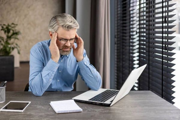 Frustrated Man sitting in front of his laptop with elbows on desk and hands cuffing his face.