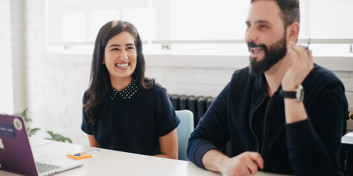 man and woman sitting at a desk smiling and talking about health insurance