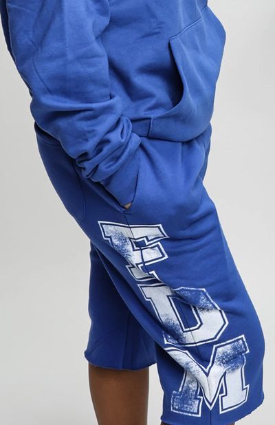 Person wearing blue sweatshorts with 'FDM' printed in white.