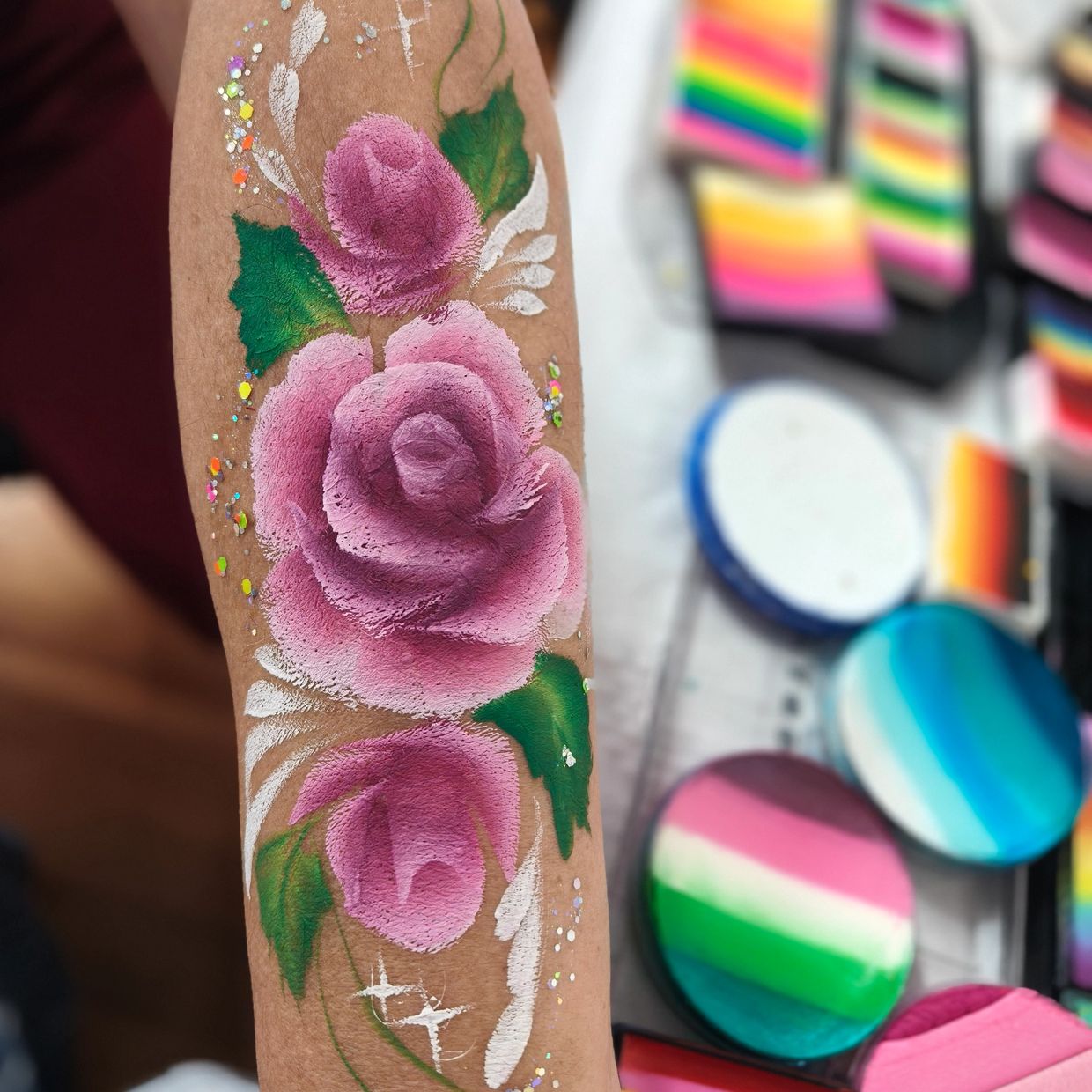 Arm painted with three pink roses and green leaves in face paint.