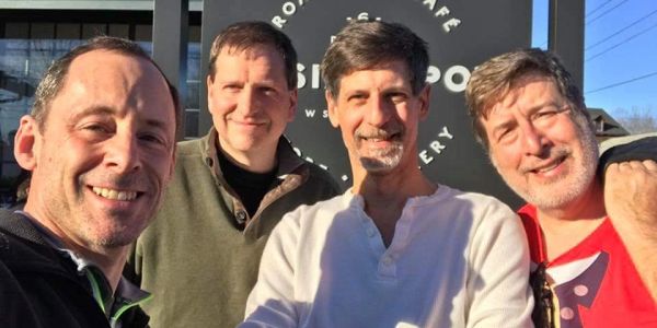 Four men smiling for a selfie outdoors.