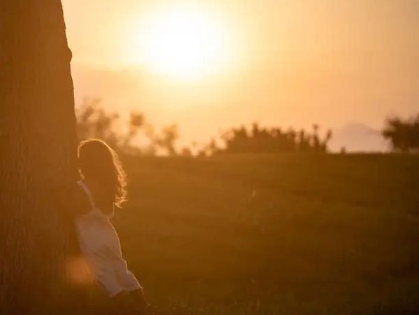 child leaning on tree at sunset — symbol of grief, emotional loss, and early soul sensitivity
