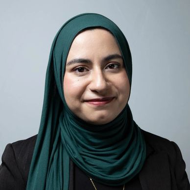 Smiling woman wearing a teal hijab and black blazer.