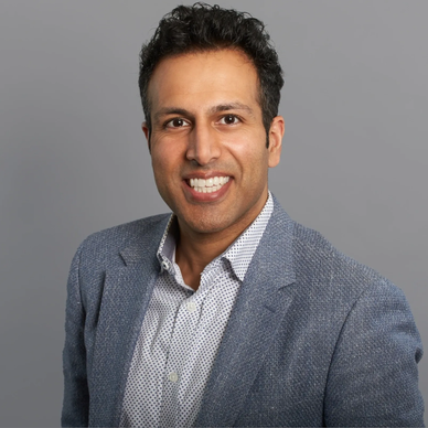 Smiling man in a blue blazer and patterned shirt.