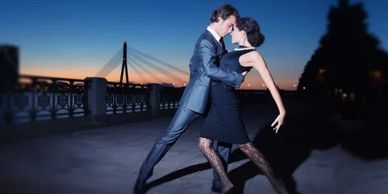 Couple dancing tango elegantly at dusk near a bridge.