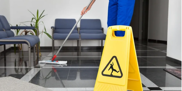 A yellow wet floor caution sign with a person mopping the floor in the background.
