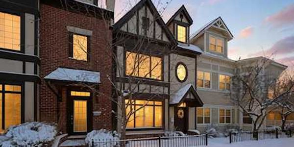 Snow-covered townhouses with warm glowing windows at dusk.