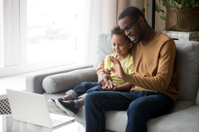 Father sitting on the couch with child and engaging with her using hand gestures.