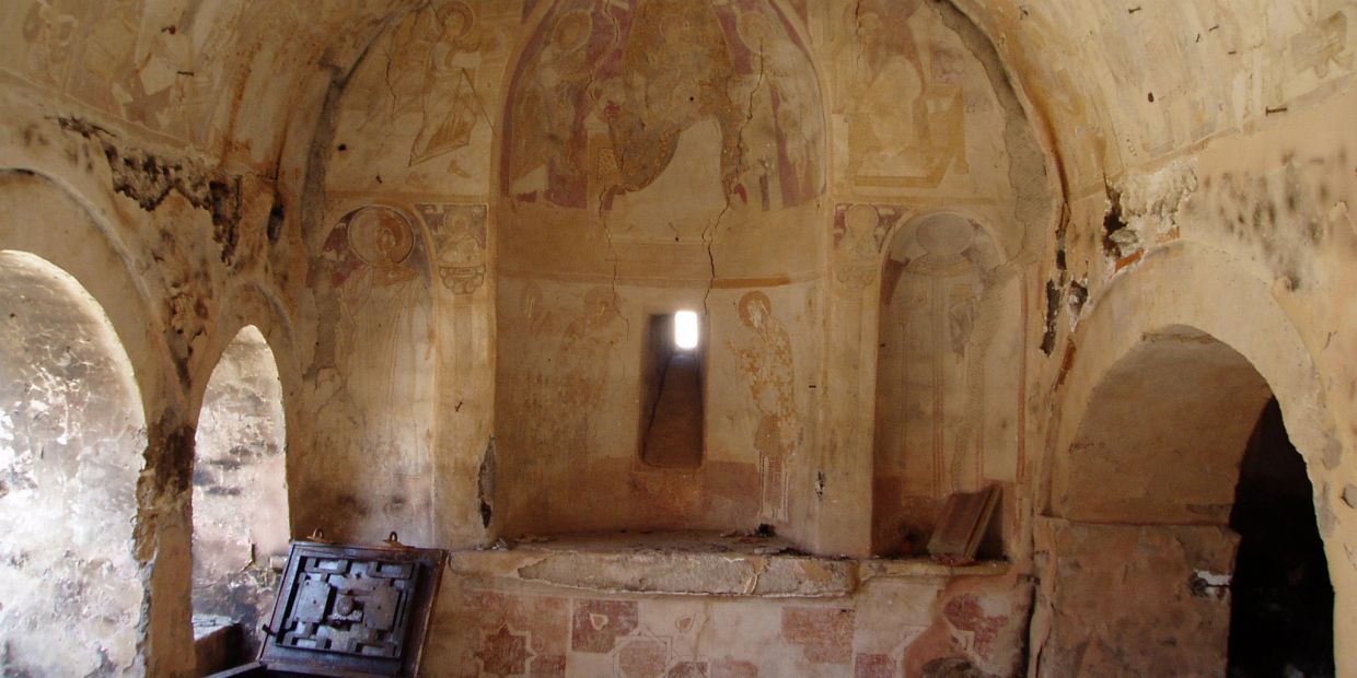 Ancient room with faded frescoes and arched windows.