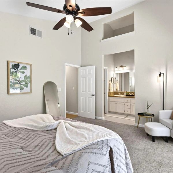 Bright bedroom with ceiling fan and open door to bathroom.