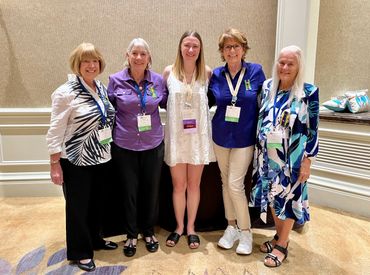 Five women standing together indoors, smiling at the camera.