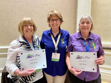 Three women smiling, two holding Tri-Psi awards.