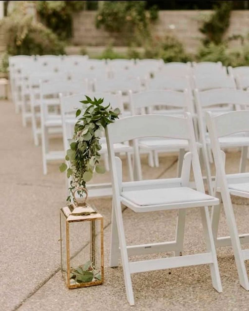 White folding chairs arranged for an outdoor event with a decorative lantern and greenery.