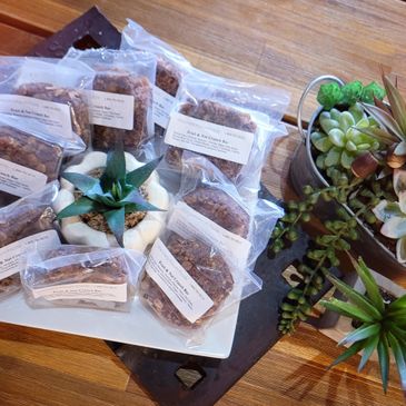 Packaged baked goods surrounding a small potted succulent on a white plate.