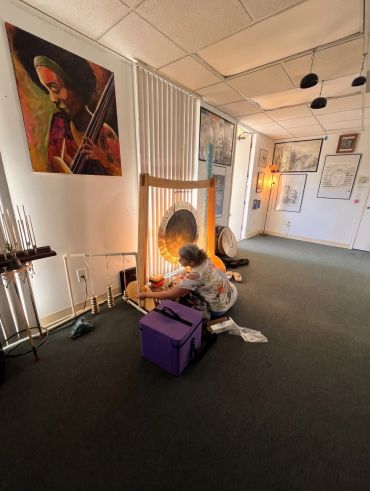 A person playing a gong in a cozy, art-filled room.