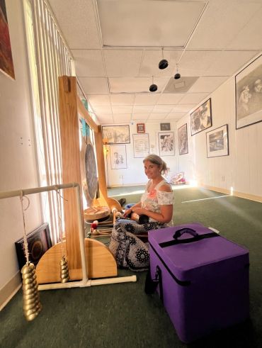 A woman sitting on the floor in a room with musical instruments and framed pictures.