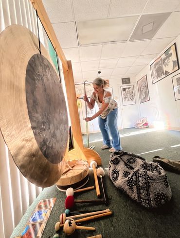 Person playing a large gong in a serene, art-filled room.