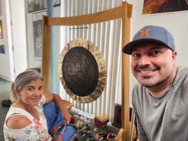 Two people smiling near a large gong in a cozy room.