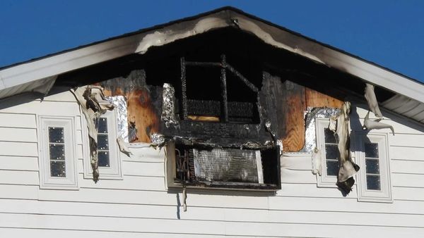 Upper part of a house shows fire damage with charred wood and melted siding.