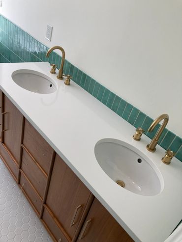 Modern double sink bathroom vanity with brass faucets and teal tile backsplash.