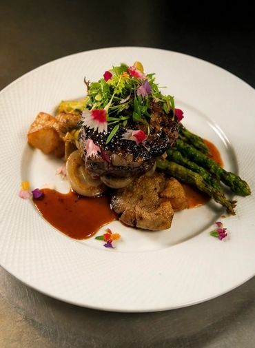 Gourmet steak with asparagus, crispy potatoes, and edible flowers.