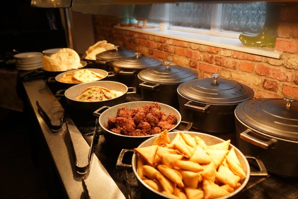 Buffet with samosas, fried items, and flatbreads in metal containers.