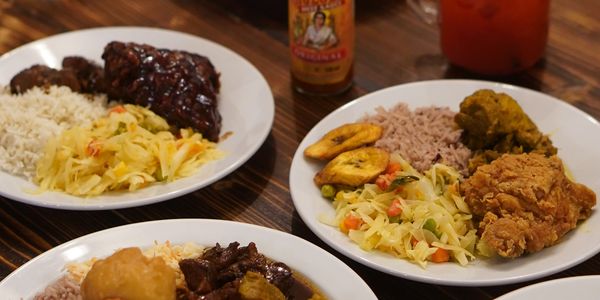 Three plates of Caribbean-inspired dishes on a wooden table.
