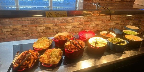 Buffet setup with various hot dishes in pots and trays on a heated counter.