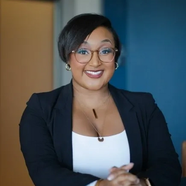 Confident woman wearing glasses and a blazer, smiling warmly.