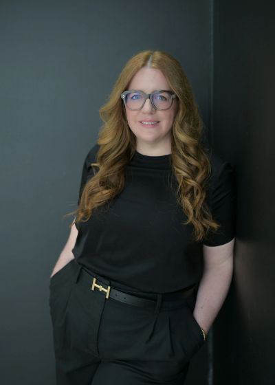 Femme souriante aux cheveux bouclés et lunettes, habillée en noir.