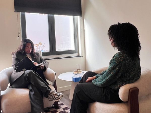 Two people engaged in a conversation in a cozy room with armchairs.