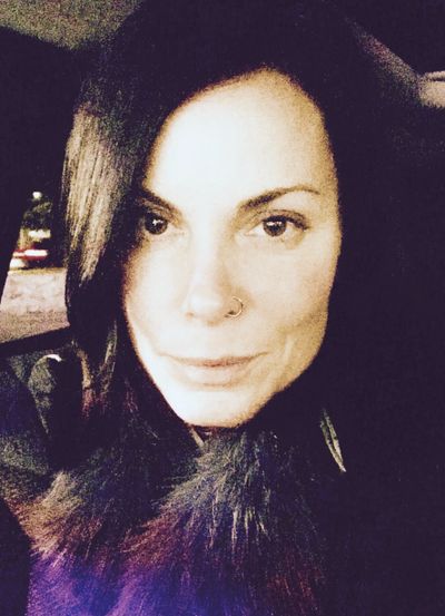 Close-up of a woman with dark hair and a nose ring, softly lit.