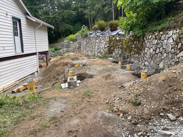 Construction site beside a house with concrete piers and stone retaining wall.