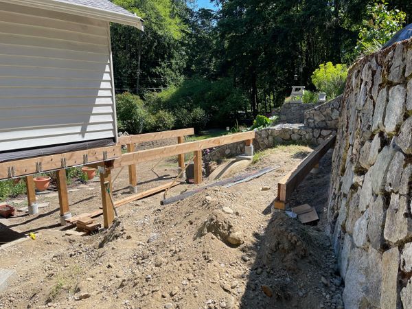 Construction of a wooden deck foundation next to a stone retaining wall.
