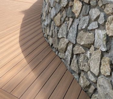 Curved wooden deck next to a stone wall.