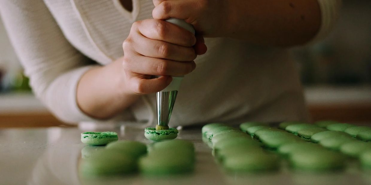 Piping Pistachio filling into a Macaron shell.