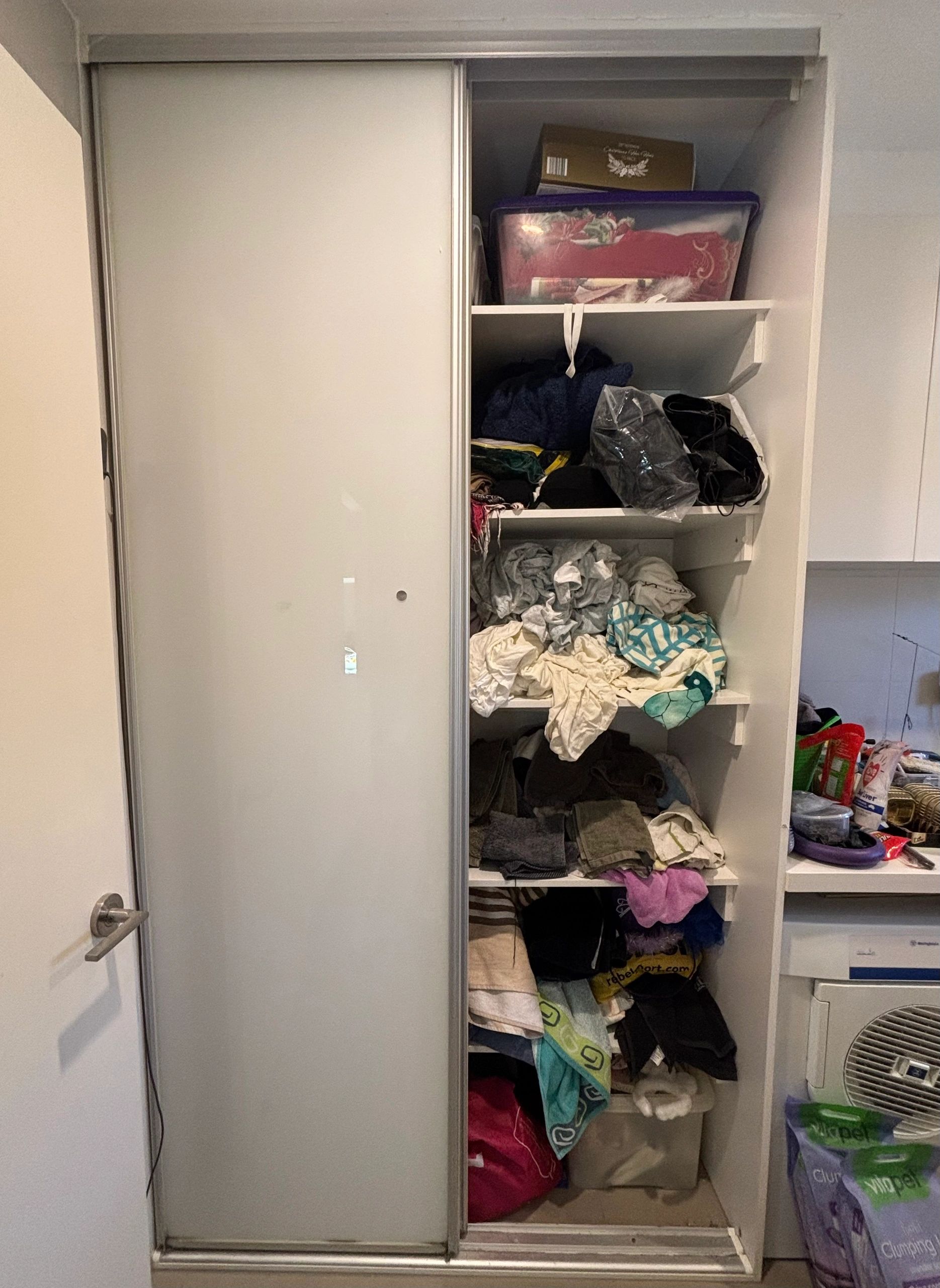 Closet with piled clothes and storage items.