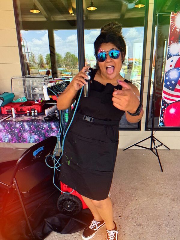 Woman in black apron playfully posing with airbrush equipment.