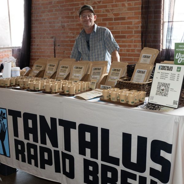 Man stands behind a table displaying coffee samples and bags at Tantalus Rapid Brew.