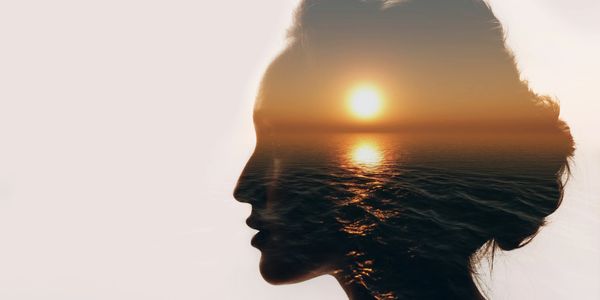 Double exposure of a woman's silhouette and a sunset over the ocean.