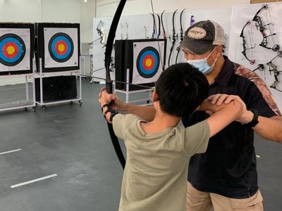 Seeds Archery 前港隊教練 Bailey Sir 手把手指導小朋友，調整標準拉弓姿勢。