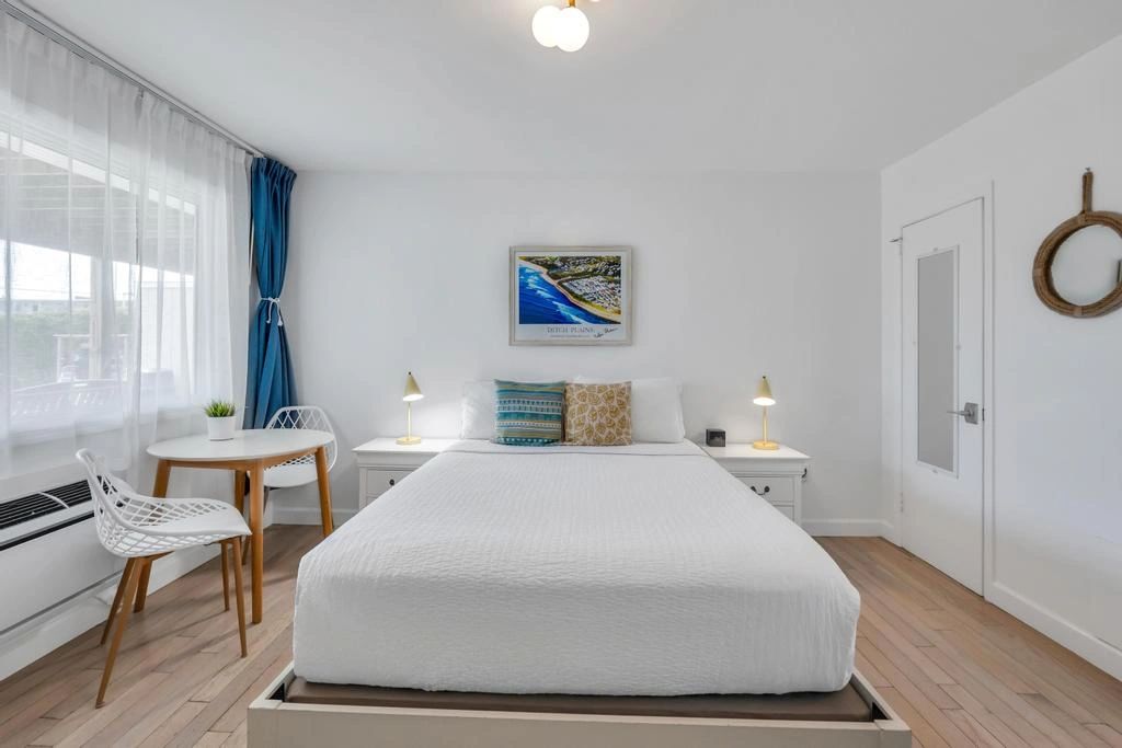 A clean and minimalist hotel room with a large bed, white furniture, and blue accents.