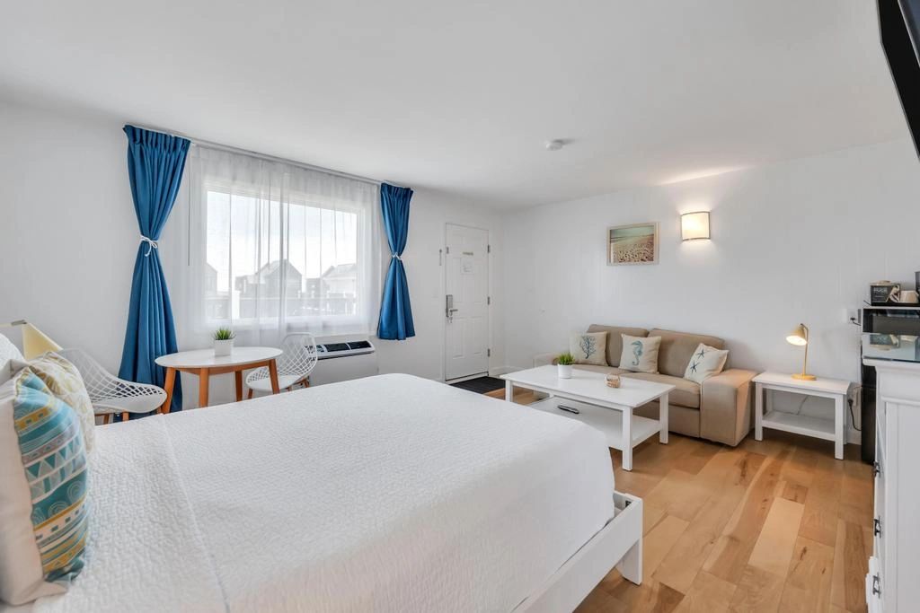 A wide view of a hotel room with a large bed, sofa, coffee table, and kitchenette.